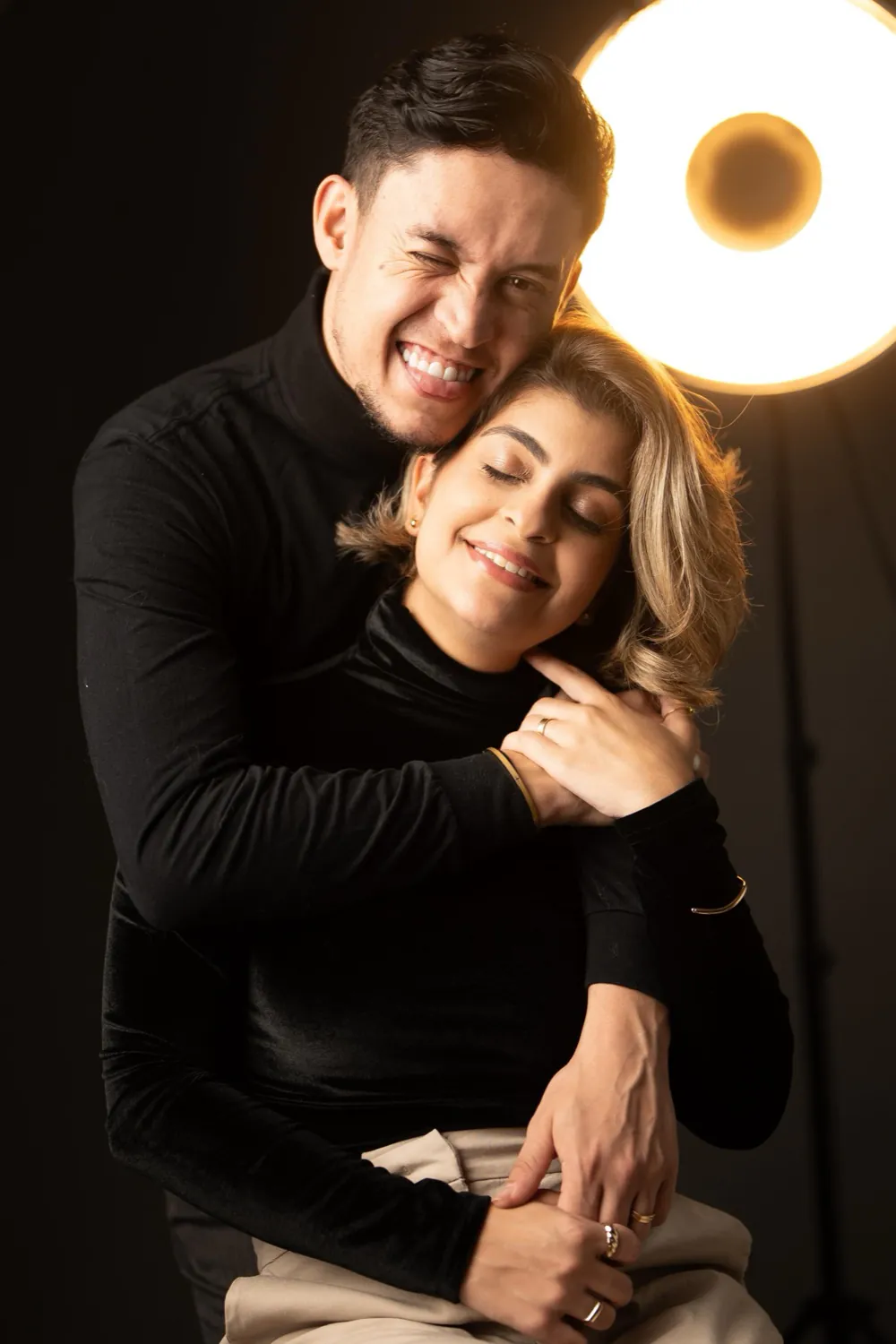 Casal sorrindo abraçado em ensaio de estúdio com luz quente