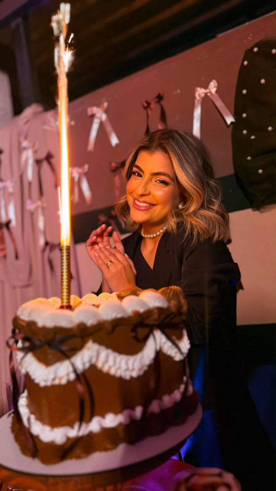 Mulher sorrindo em festa de aniversário com bolo e vela faísca, foto noturna com celular