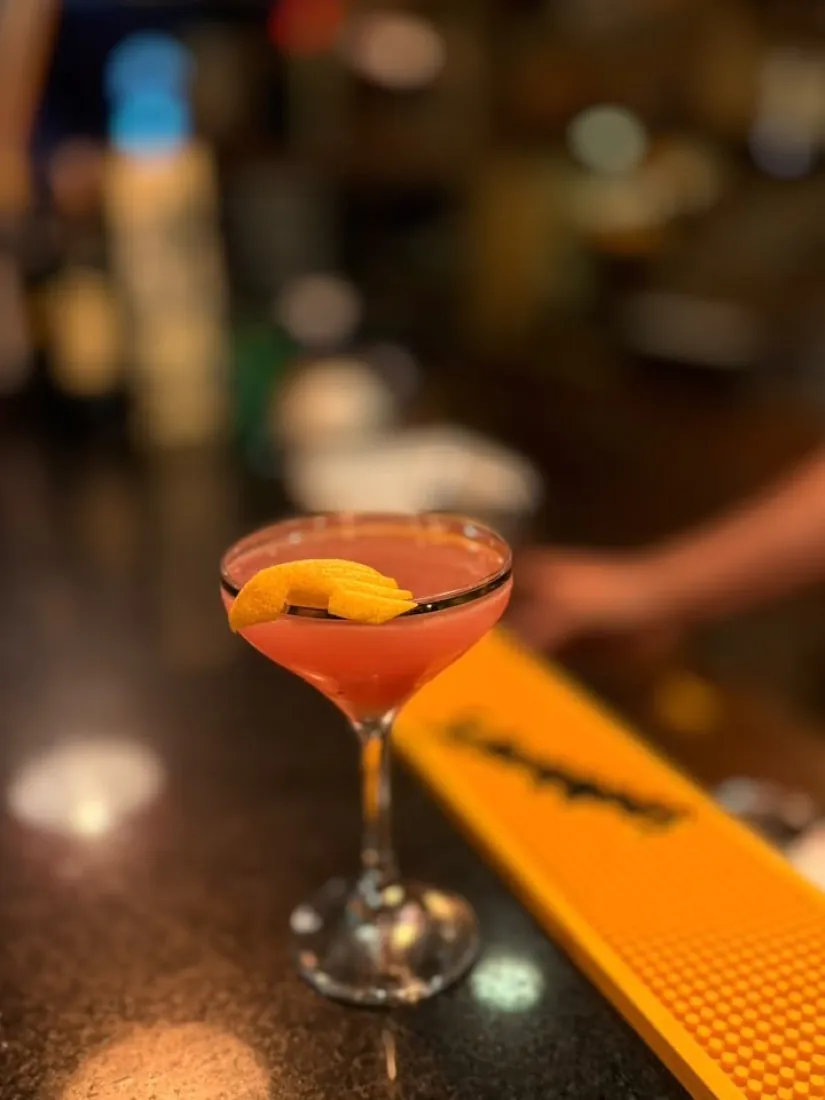 Drink autoral com casca de laranja no balcão de um bar, foto noturna feita com celular
