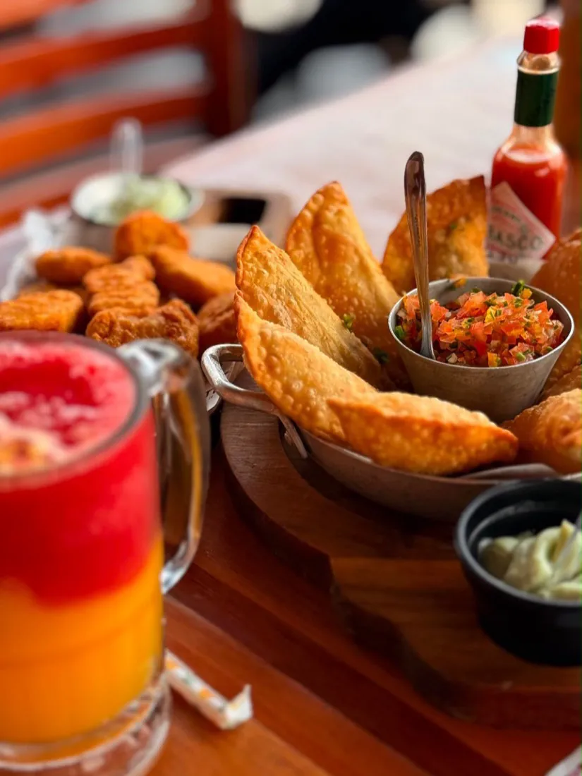 Mesa de boteco com pastéis, molhos e suco colorido, foto gastronômica feita com celular