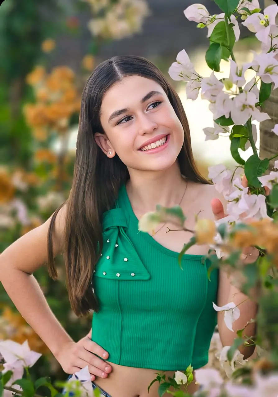 Retrato de menina sorrindo entre flores, blusa verde, foto feita com celular